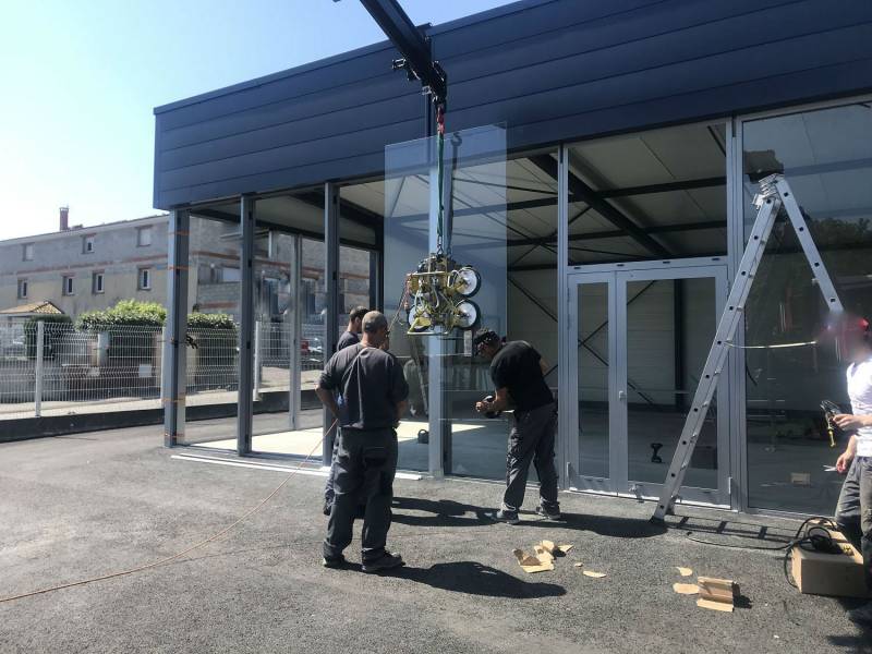 Mise en place des vitrages par camion grue sur vitrine de magasin en aluminium en cours de réalisation